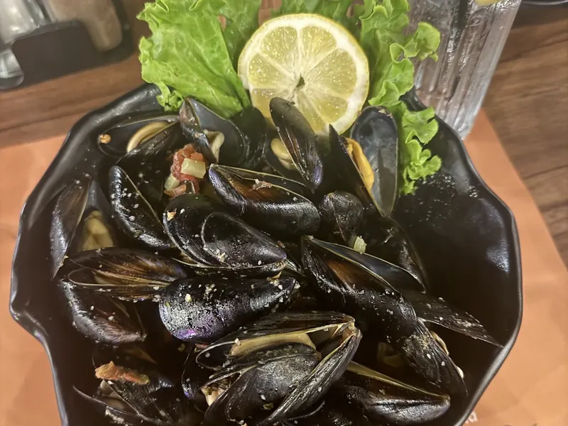 A black pot of mussels topped with lemon and lettuce