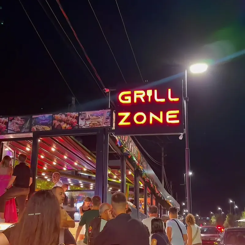 The lit Grill Zone sign above the terrace at night, with guests arriving