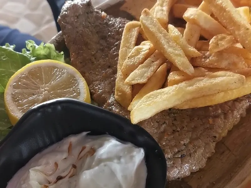 Grilled beef steak with fries, lemon and a dish of tzatziki